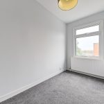 Empty grey carpeted room with window and radiator.