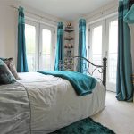 Cosy bedroom with teal accents and large windows.