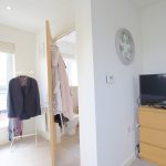 Bedroom with TV and clothes hanger near window.