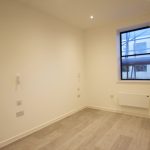 Empty room with wooden flooring, window view outside.