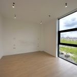 Bright empty room with large window and wooden floor.