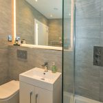 Modern bathroom with shower and mirrored lighting.