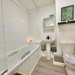 Modern bathroom with white tiles and wooden floor.