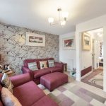 Cosy living room with purple sofas and patterned wallpaper.