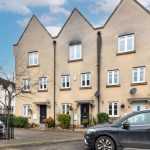 Row of modern terraced houses with parked cars.