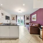 Modern kitchen with purple feature wall and sofa.