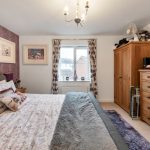 Cosy bedroom with bed, artwork, window, and wooden furniture.