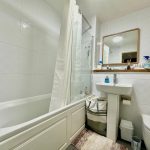 Modern white bathroom with bathtub, sink, and mirror.