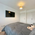 Bedroom with grey bedding and wall-mounted TV.