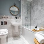 Modern bathroom with marble tiles and round mirror.