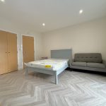 Spacious bedroom with bed and grey sofa.