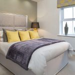 Modern bedroom with yellow cushions and grey throw.