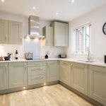 Modern kitchen with green cabinets and wooden floor.