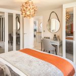 Modern bedroom with orange accents and mirrored wardrobe.