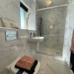 Modern bathroom with marble tiles and glass shower.