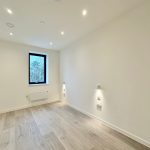 Spacious empty room with wooden flooring and window.