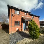 Two-storey brick house with garden under cloudy sky.