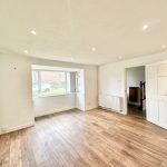 Spacious empty room with wooden flooring, white walls.