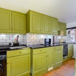 Modern kitchen with green cabinets and wooden floor.