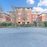 Red brick apartment building with trees and shrubs.