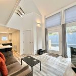 Modern living room with open kitchen and large windows.