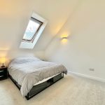 Modern attic bedroom with skylight and grey bedding.