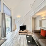 Modern living room with large windows and staircase.