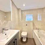 Modern bathroom with white fixtures and beige tiles.