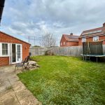 Backyard with patio, grass, chairs, trampoline, brick house.